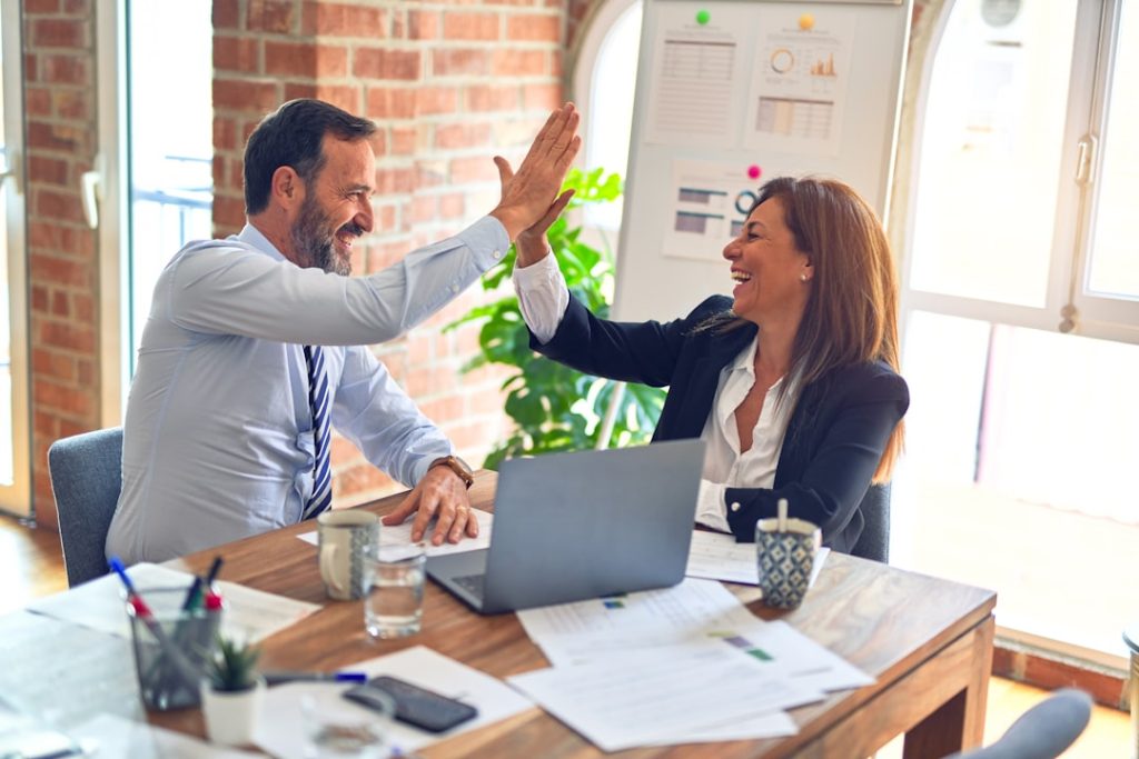 Two people sitting and working on a table together and giving a high five
