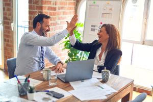 Two people sitting and working on a table together and giving a high five